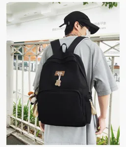 Close-up detail of casual black campus backpack featuring cute bear pendant and logo patch.