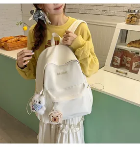 Detailed view of casual white campus backpack with cute plush pendants worn by model.
