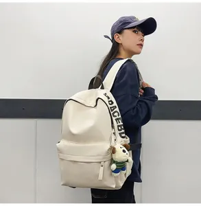 Close-up detail of stylish white PU leather backpack for women with cute dog plush pendant.