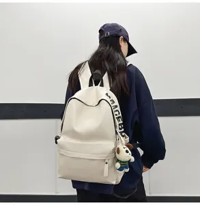 Detail view of a stylish white PU leather backpack with side lettering and a cute plush charm.