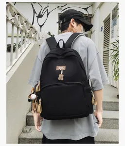 Black canvas school backpack for students with cute bear pendant and large capacity.