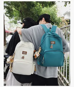 Outdoor lifestyle scene showing campus backpacks with cute bear pendants and solid color design.