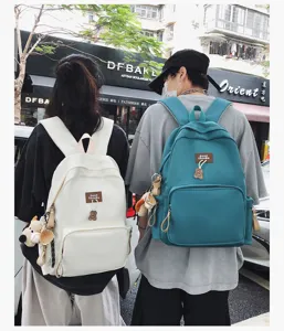 Outdoor street scene detail view of solid color campus school backpack with cute bear pendant.
