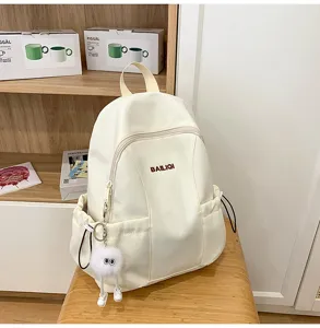 Detailed view of the casual off-white waterproof canvas backpack with cute plush keychain.