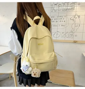Light yellow casual school backpack detail view with cute plush pendants and front pocket.