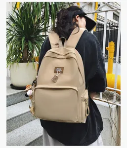 Detailed shot of a casual khaki canvas backpack with bear pendant and front pocket outdoors.