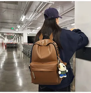 Brown PU leather backpack for women, casual school bookbag with cute plush dog pendant.
