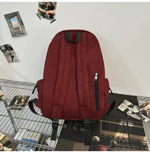 Detail view of dark red canvas backpack with shoulder straps and vertical zipper pocket.