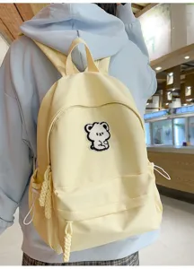 Detail shot of a cute minimalist yellow student backpack featuring a sweet bear patch design.