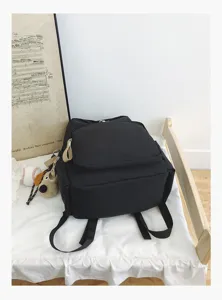 Detail shot of a minimalist black campus backpack with zipper pockets and cute plush pendant.