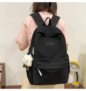Detailed view of this minimalist black school backpack, showing back wear and cute plush pendant.
