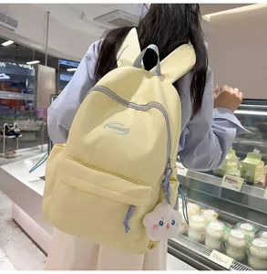 Detalle de mochila amarilla bonita, bolso escolar estético con orejas de conejo y colgante.