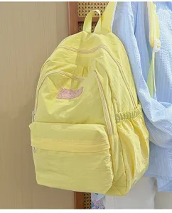 Detail view of a light yellow minimalist school backpack with multiple zip compartments.