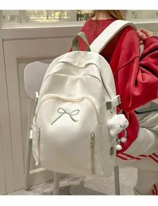Detail view of the cute white student backpack with green bow embroidery and plush bear pendant.