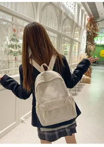 Back view of woman wearing beige corduroy backpack in shopping street scene detail.