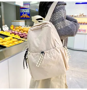 Detail view of beige nylon backpack showing front drawstring pocket and shoulder straps.