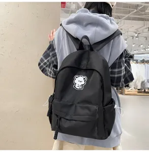 Detail view of the black canvas backpack featuring a cute white bear patch and daily scene.