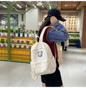 Stylish white canvas school backpack for teen girls with cute bear patch, casual daily bag.