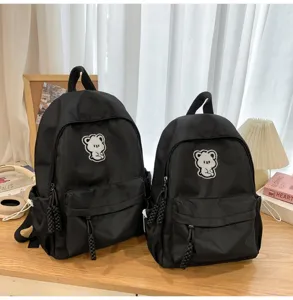 Close-up detail of black school backpacks featuring cute bear embroidery and practical pockets.