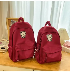 Detailed view of stylish burgundy school backpacks with cute bear patches, placed on a wooden desk.