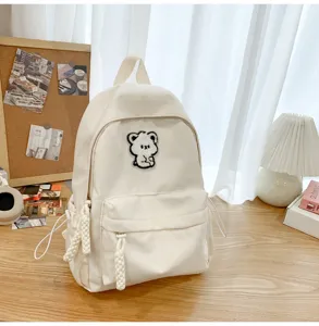 Simple white school backpack for teen girls with cute bear patch, stylish daily casual bag.