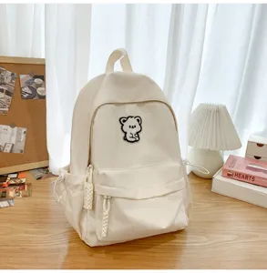 Casual white backpack detail showing cute bear patch, front pocket and smooth zipper design.