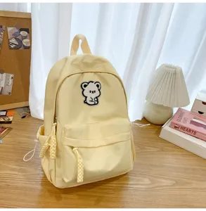 Detail view of light yellow canvas backpack featuring cute bear patch and cozy desk background.