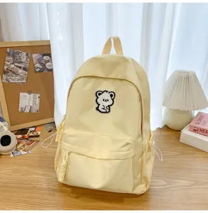 Detail view of a cute yellow backpack with bear patch and cozy aesthetic desk setting.