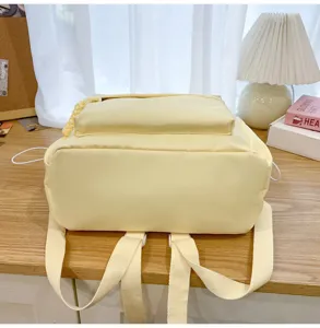 Close-up detail of light yellow canvas backpack featuring dual shoulder straps and front pocket.