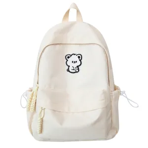 Minimalist beige canvas backpack for women, cute bear patch schoolbag with multiple pockets.