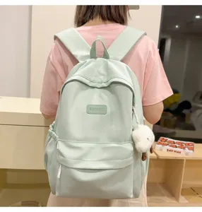 Detail view of a solid color light green school backpack with front pocket and charm.