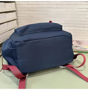 Vista detallada de mochila casual de nailon azul oscuro con correas rojas sobre superficie verde.