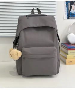 Detailed view of the solid grey nylon backpack with cute bear pendant and daily school props.