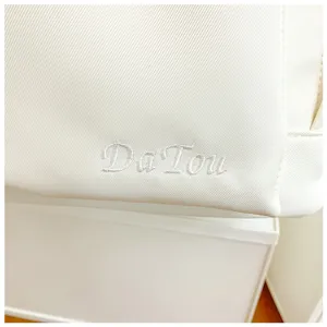 Close-up detail of white canvas backpack with stylish letter embroidery design, minimalist.