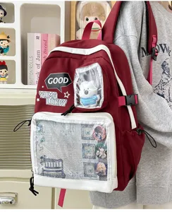 Detalle de mochila ita roja con ventana transparente, colgante de oso y chapas de anime.