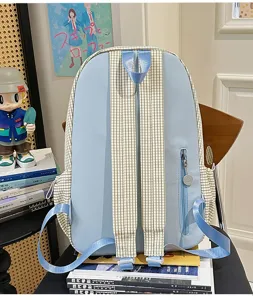 Detailed view of light blue canvas backpack with plaid side panels and unique zipper pull.