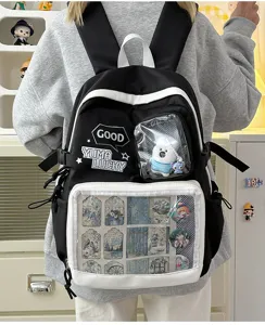 Mochila ita en blanco y negro con ventana transparente, chapas de anime y colgante de peluche.
