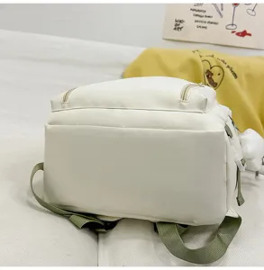 Close up detail of white canvas backpack showing green adjustable straps and pocket.