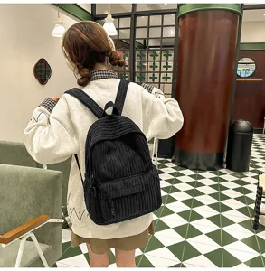Detail view of the black corduroy backpack worn by a model in a stylish indoor café setting.