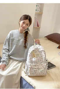 Close-up detail of the floral print student backpack featuring cute plush pendant and pockets.