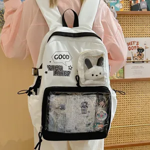 Mochila Ita de lona blanca y negra con bolsillo frontal transparente para pines y peluche.
