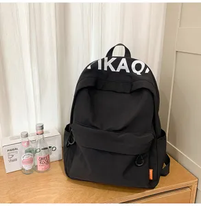 Minimalist black casual school backpack detail view showcasing front zipper pocket and strap.