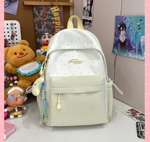 Close-up of white star pattern school backpack with front pocket and charms in a room.