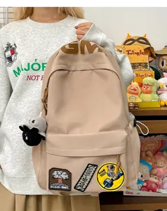 Korean style large capacity beige canvas backpack with cute patches and doll pendant for students.