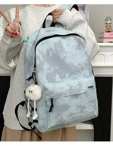 Detail view of the light blue tie-dye backpack showing front pocket, zipper, and fluffy doll charm.