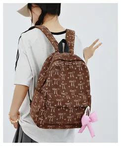 Detail view of brown corduroy backpack featuring white bows and a cute pink pendant charm.