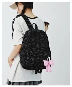 Detail view of black bow print backpack worn by model, showing texture and pink pendant.