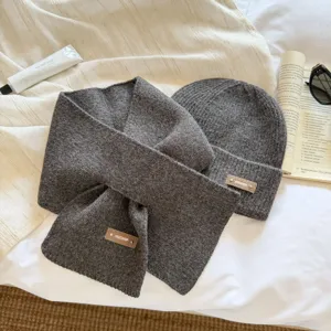 Detailed close-up of dark gray knitted scarf and matching beanie set on white fabric.