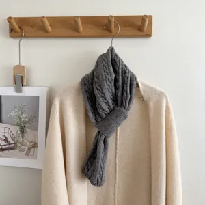 Detailed view of a cozy grey cable knit cross scarf hanging on a wooden rack with a cardigan.