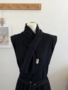 Detail view of the black cross knit scarf on a mannequin, showing soft texture and cozy design.